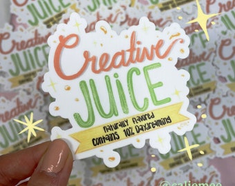 May include: A white sticker with the text "Creative Juice" in a colourful, handwritten font. The text is surrounded by small gold stars and the sticker has a yellow banner at the bottom that reads "Naturally flavoured Contains 10% Daydreaming".