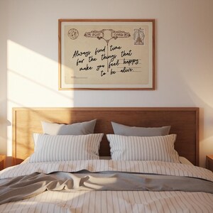 Puede incluir: Una postal enmarcada de estilo vintage con el texto "Always find time for the things that make you feel happy to be alive." La postal se muestra encima de una cama con almohadas a rayas y un cabecero de madera.