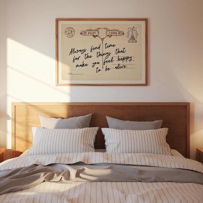Puede incluir: Una postal enmarcada de estilo vintage con el texto "Always find time for the things that make you feel happy to be alive." La postal se muestra encima de una cama con almohadas a rayas y un cabecero de madera.