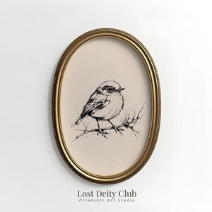 Peut inclure: Une impression ovale encadrée d'or avec un dessin en noir et blanc d'un oiseau sur une branche. L'œuvre d'art est placée sur un fond beige. Le texte "Lost Deity Club Printable Art Studio" est en bas.