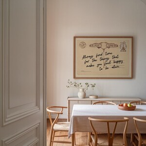 Puede incluir: Una impresi&oacute;n enmarcada de postal vintage con el texto "Always find time for the things that make you feel happy to be alive." La impresi&oacute;n se muestra encima de una mesa de comedor, con sillas de madera y un mantel blanco.