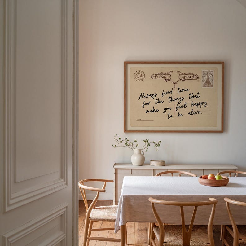 Puede incluir: Una impresi&oacute;n enmarcada de postal vintage con el texto "Always find time for the things that make you feel happy to be alive." La impresi&oacute;n se muestra encima de una mesa de comedor, con sillas de madera y un mantel blanco.