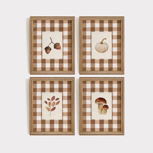 Op de afbeelding: Vier ingelijste aquarelprints met een herfstthema. Elke print toont een andere afbeelding: eikels, een pompoen, herfstbladeren en paddenstoelen. Het kunstwerk staat tegen een crèmekleurige achtergrond en is omlijst met een bruin-wit geruit patroon.