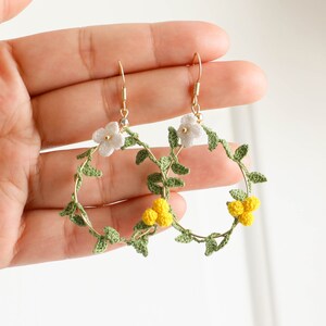 May include: A pair of gold hoop earrings with crocheted green leaves and white and yellow flowers.