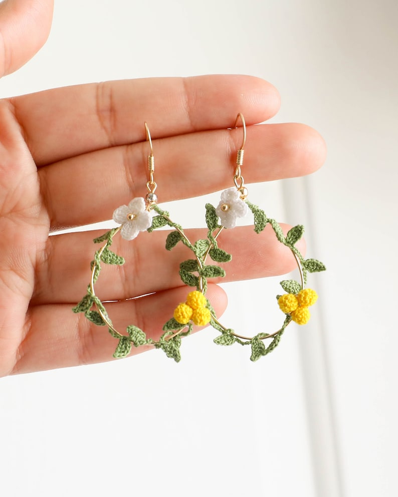 May include: A pair of gold hoop earrings with crocheted green leaves and white and yellow flowers.