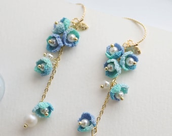 May include: A pair of long, delicate earrings featuring a cluster of blue and turquoise crocheted flowers with pearl accents. The earrings are suspended from a gold chain.