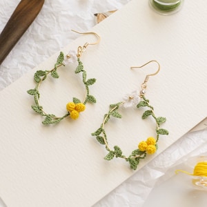 May include: A pair of gold hoop earrings with crocheted green leaves and white and yellow flowers.