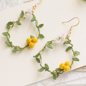 May include: A pair of gold hoop earrings with crocheted green leaves and white and yellow flowers.