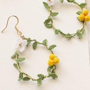 May include: A pair of gold hoop earrings with crocheted green leaves and white and yellow flowers.