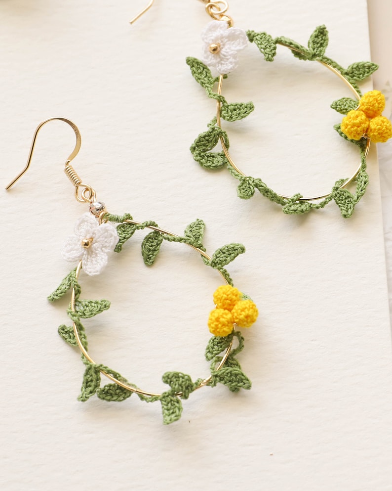 May include: A pair of gold hoop earrings with crocheted green leaves and white and yellow flowers.