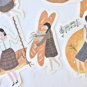 May include: Watercolor stickers featuring illustrations of women with baked goods. One woman swings on a baguette swing, another carries baguettes, and a third sits near musical notes. The stickers have a vintage, hand-drawn aesthetic.