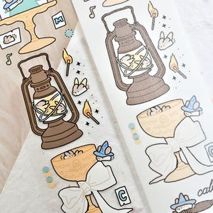 May include: Two strips of decorative tape with whimsical illustrations. One strip features a brown lantern, a chalice with a bow, and a cake. The other strip has a similar design with a lantern, chalice, and the words "call me".