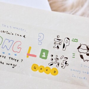 Może przedstawiać: Przezroczysta taśma washi z kolorowymi, ręcznie rysowanymi ilustracjami i tekstem. Tekst zawiera "SONG", "How do I love three?", "Let me count the ways", "GOOD" i "1". Ilustracje obejmują ananasa, krowę i znak zapytania.