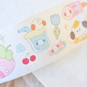 May include: A white washi tape with a repeating pattern of cartoon animals, fruit, and other cute designs. The tape features a strawberry, cherries, a dog drinking from a glass, a dog with an ice cream cone, a dog with a spoon, and a dog with a popsicle.