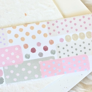 Pode incluir: Uma folha de fita washi com um design de patchwork que apresenta vários padrões de bolinhas rosa, brancas, cinzas e bege.