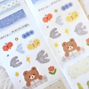 Op de afbeelding: Twee vellen stickers met een natuurthema. De stickers bevatten een bruine beer, vlinders, vogels, sterren en wolken. De tekst op de stickers luidt "early mornings" en "o day".