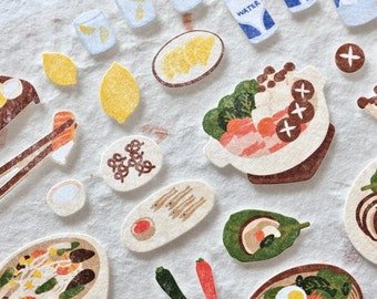 May include: A collection of illustrated food stickers featuring Japanese cuisine, including sushi, ramen, and hot pot. The stickers are printed on a textured paper and have a rustic, hand-drawn style.