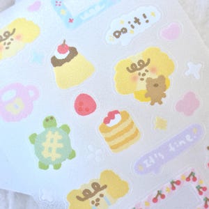 Puede incluir: Una hoja de pegatinas coloridas con personajes de dibujos animados, postres y frases como "Do it!" y "It's fine." Las pegatinas están sobre un fondo blanco.