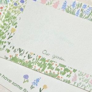 Könnte beinhalten: Zwei weiße Karten mit einem floralen Rand. Die obere Karte hat einen leeren Platz mit dem Text "Our garden." Die untere Karte hat den Text "We have some flo" mit ein paar gezeichneten Blumen auf der rechten Seite.