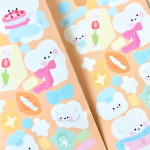 May include: A sheet of stickers featuring cute cartoon clouds with different expressions and accessories. The stickers are on a peach background with various other illustrations, including stars, flowers, and bows.