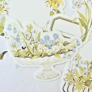 May include: A collection of floral-themed stickers featuring watercolor illustrations. The stickers showcase various flowers, including pansies, lilies, and hydrangeas, in soft pastel colors. The designs are arranged in decorative arrangements.