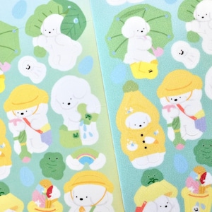 May include: A sheet of stickers featuring illustrations of white fluffy dogs in various poses, including holding umbrellas, watering plants, and wearing raincoats. The stickers are on a light blue background with green leaves and other nature-themed elements.