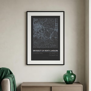 Op de afbeelding: Een ingelijste kaartafdruk van de Universiteit van North Carolina, Chapel Hill, in een zwart frame. De kaart is een gedetailleerd, lichtblauw en wit ontwerp op een donkere achtergrond. De tekst "UNIVERSITY OF NORTH CAROLINA CHAPEL HILL" wordt hieronder weergegeven.