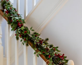 Könnte beinhalten: Ein festlicher Weihnachtskranz schmückt ein Holztreppengeländer. Der Kranz besteht aus grünem Laub, roten Beeren und Tannenzapfen. Die Treppe hat weiße Baluster und einen Holzhandlauf.