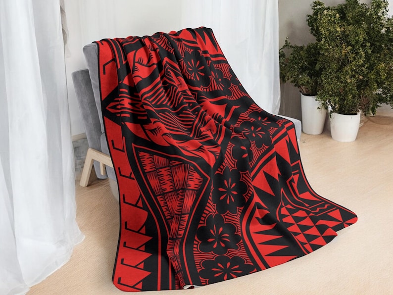 Puede incluir: Manta de tiro roja y negra con un patr&oacute;n de inspiraci&oacute;n polinesia. El patr&oacute;n presenta formas geom&eacute;tricas, flores y una figura humana estilizada.