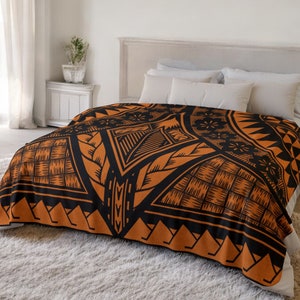 Puede incluir: Una manta de forro polar con estampado geom&eacute;trico en negro y naranja. La manta est&aacute; doblada y se muestra en una cama con almohadas blancas.