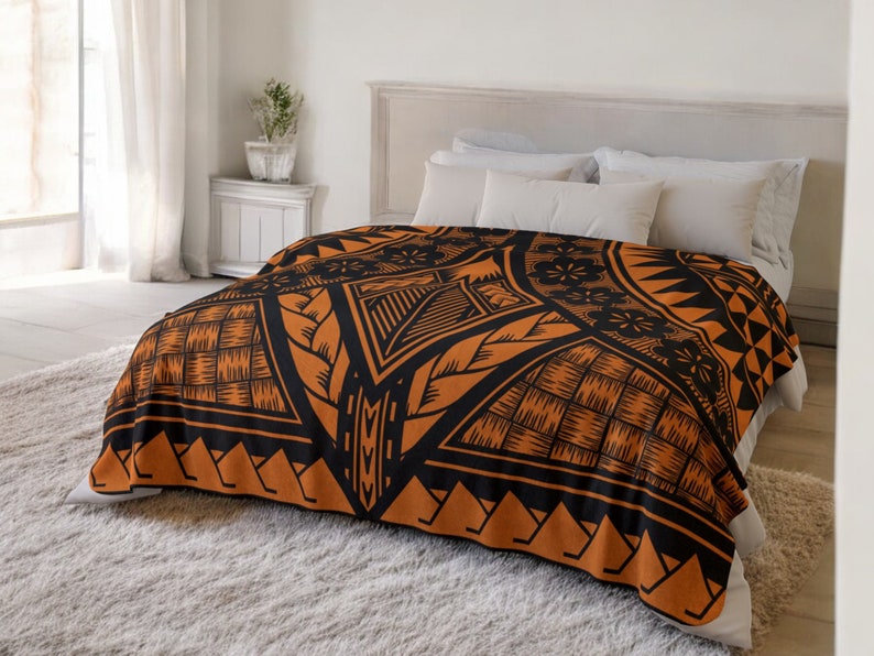 Puede incluir: Una manta de forro polar con estampado geom&eacute;trico en negro y naranja. La manta est&aacute; doblada y se muestra en una cama con almohadas blancas.