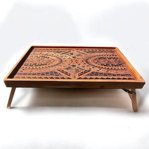 May include: A wooden serving tray with foldable legs. The tray features a geometric pattern carved into the wood.