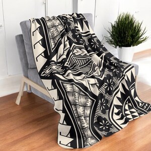 Puede incluir: Manta de tiro en blanco y negro con un patr&oacute;n geom&eacute;trico que presenta flores y olas estilizadas. La manta est&aacute; doblada y drapeada sobre una silla.