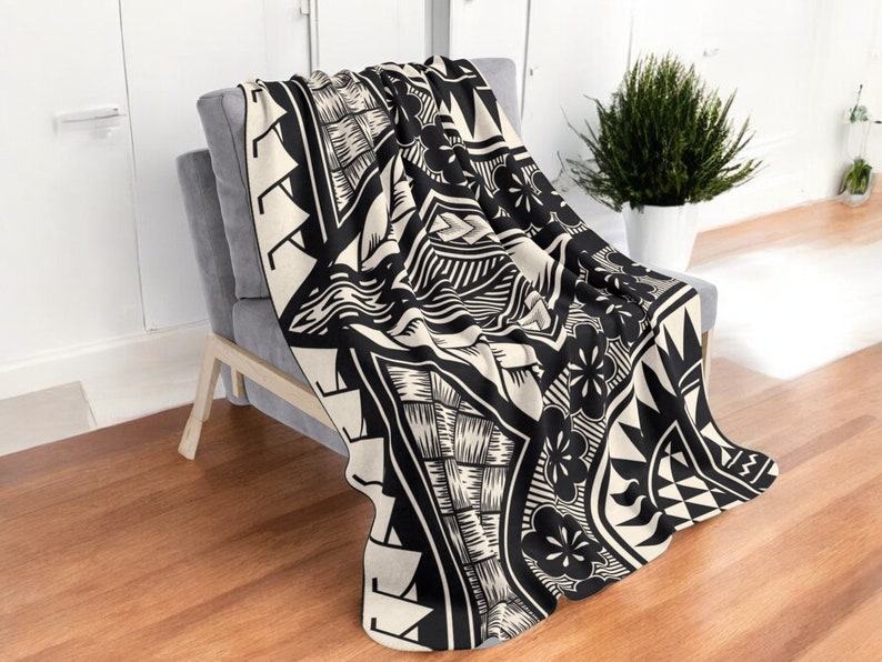 Puede incluir: Manta de tiro en blanco y negro con un patr&oacute;n geom&eacute;trico que presenta flores y olas estilizadas. La manta est&aacute; doblada y drapeada sobre una silla.