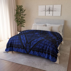 Puede incluir: Una manta de franela azul y negra con un dise&ntilde;o geom&eacute;trico. La manta est&aacute; doblada en una cama con almohadas blancas.