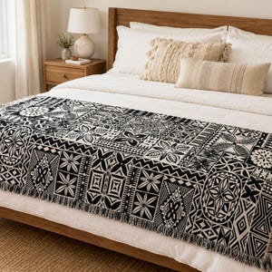 May include: A rectangular woven bed runner featuring a high-contrast black and white geometric pattern with repeating tribal-inspired motifs, including star-like shapes, zigzags, and diamond designs, finished with a fringed edge on both ends.