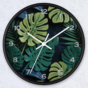 May include: A black round clock with white hands and a dark blue background. The clock face features a tropical leaf design with green and yellow leaves.