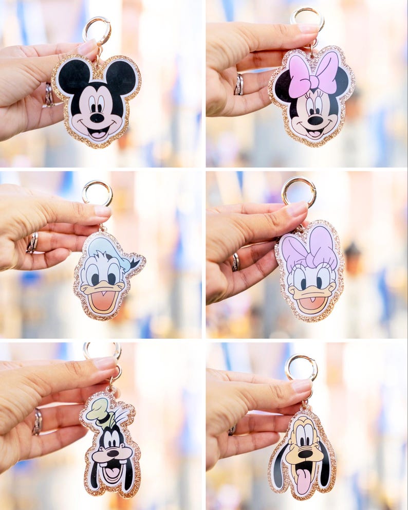 May include: A collection of character keychains featuring Mickey Mouse, Minnie Mouse, Donald Duck, Daisy Duck, and Goofy. Each keychain has a gold glitter border and a gold keyring. The characters are in color with black, white, pink, blue, and yellow.