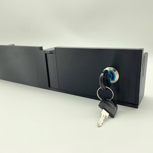 May include: A black metal box with a keyhole and a key inserted. The box has a hinged lid and a latch.