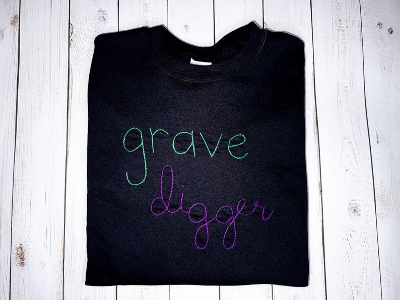 Pu&ograve; includere: Felpa nera con le parole "grave digger" ricamate in filo verde e viola.