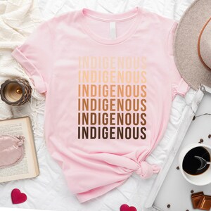 Może przedstawiać: R&oacute;żowy T-shirt z napisem "Indigenous" powt&oacute;rzonym sześć razy w gradiencie brązowych odcieni.