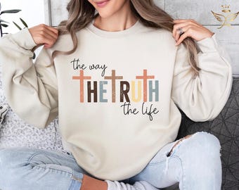 May include: A cream-colored sweatshirt with the text "the way the truth the life" printed on the front. The text is surrounded by three stylized crosses in shades of brown, orange, blue, and yellow.