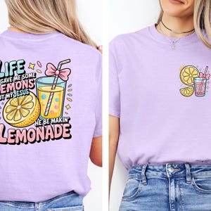 May include: A light purple t-shirt with a graphic design featuring a lemon, a glass of lemonade, and the text "Life gave me some lemons but my Jesus he be makin' lemonade." A smaller version of the design is on the front.