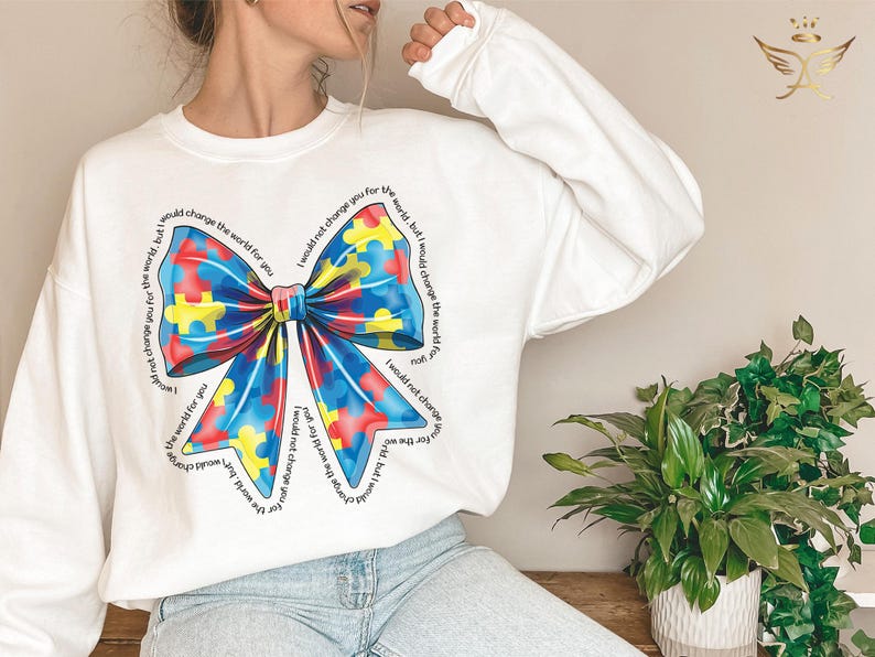 Puede incluir: Sudadera blanca con un dise&ntilde;o de lazo de piezas de rompecabezas azules, rojas y amarillas. El texto alrededor del lazo dice "No te cambiar&iacute;a por el mundo, pero cambiar&iacute;a el mundo por ti".