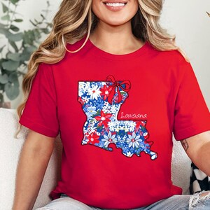 May include: Red t-shirt with a floral print of the state of Louisiana and the word "Louisiana" printed on the shirt.