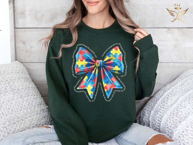 Puede incluir: Una sudadera verde oscuro con un gran lazo colorido hecho de piezas de rompecabezas. El lazo est&aacute; rodeado por el texto "No te cambiar&iacute;a por el mundo, pero cambiar&iacute;a el mundo por ti".