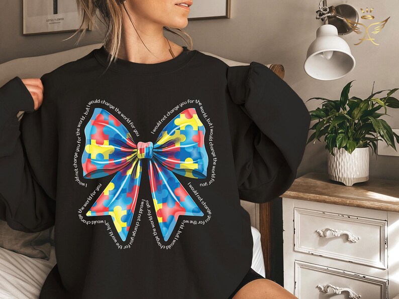 Puede incluir: Sudadera negra con un lazo de piezas de rompecabezas de colores y el texto "No te cambiar&iacute;a por el mundo, pero cambiar&iacute;a el mundo por ti".