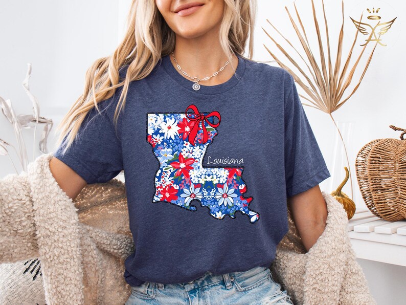 May include: A navy blue t-shirt with a floral print of the state of Louisiana. The print includes a red bow and the word "Louisiana".