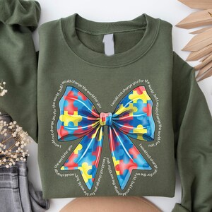 Puede incluir: Una sudadera verde con un lazo de piezas de rompecabezas de colores y el texto "No te cambiar&iacute;a por el mundo, pero cambiar&iacute;a el mundo por ti".