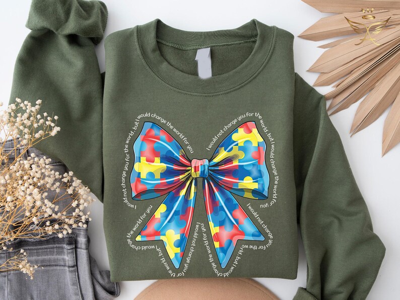 Puede incluir: Una sudadera verde con un lazo de piezas de rompecabezas de colores y el texto "No te cambiar&iacute;a por el mundo, pero cambiar&iacute;a el mundo por ti".